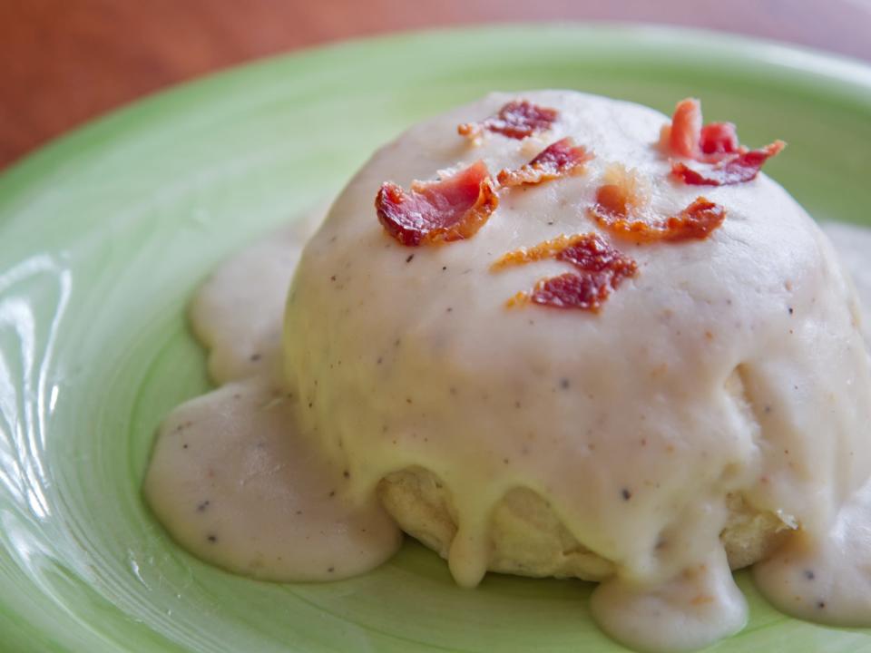 Biscuit covered in gravy and bacon bits on a green plate.