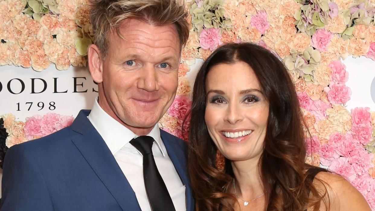 Gordon Ramsay in a suit with wife Tana against a backdrop of pink flowers