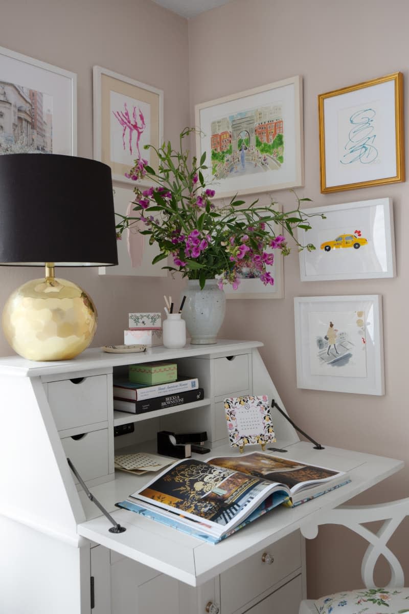 Corner gallery wall, fold down white secretary desk, purple floral arrangement, black lamp shade on round gold base