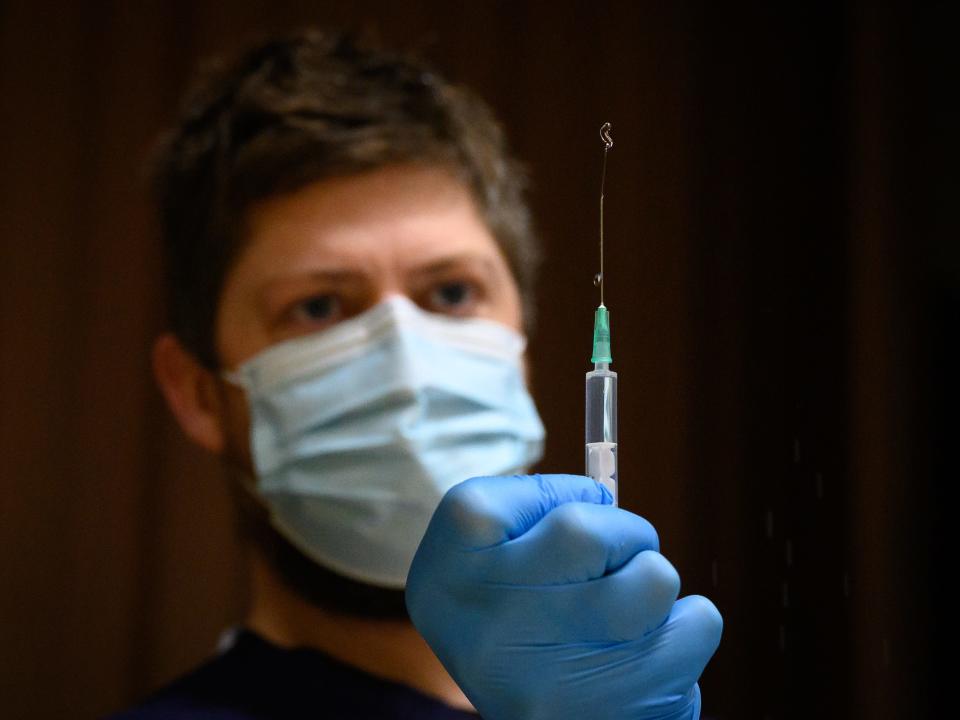 A paramedic flushes a syringe before preparing a shot of the Pfizer/BioNTech vaccine as people wait at a COVID-19 vaccination centre on December 16, 2020 in Chertsey, England.