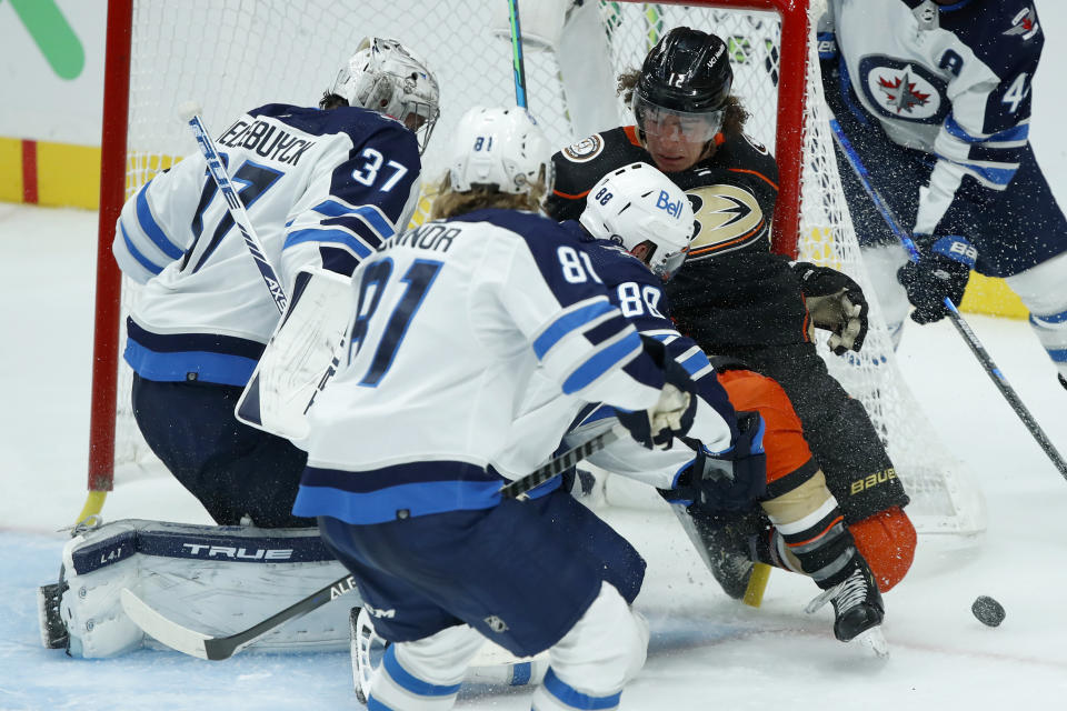 Anaheim Ducks left wing Sonny Milano, right, gets pushed away from the goal by Winnipeg Jets defenseman Nate Schmidt (88) as goaltender Connor Hellebuyck, left, and left wing Kyle Connor (81) defend during the third period of an NHL hockey game in Anaheim, Calif., Tuesday, Oct. 26, 2021. (AP Photo/Alex Gallardo)