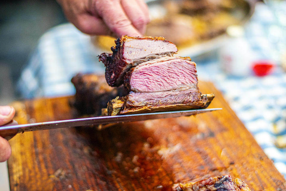 Person slicing through smoked meat on a wooden cutting board