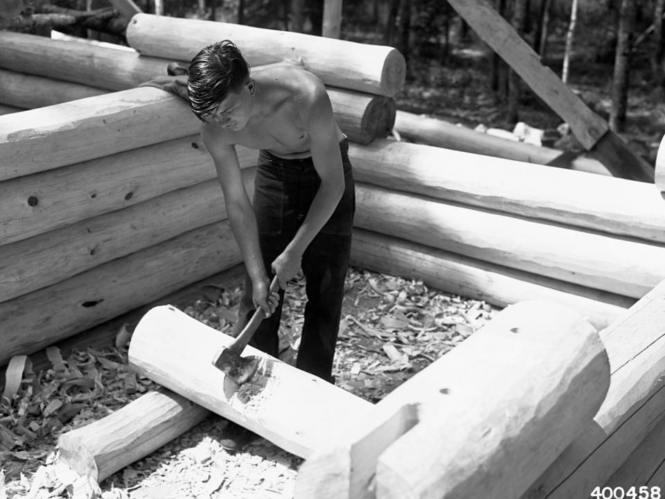 A black and white photo of a young man hitting wood with an axe.