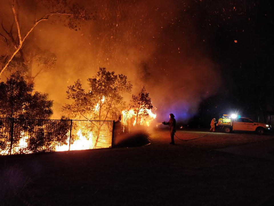 A person holds a hose up to a burning fence at night in Queensland. 