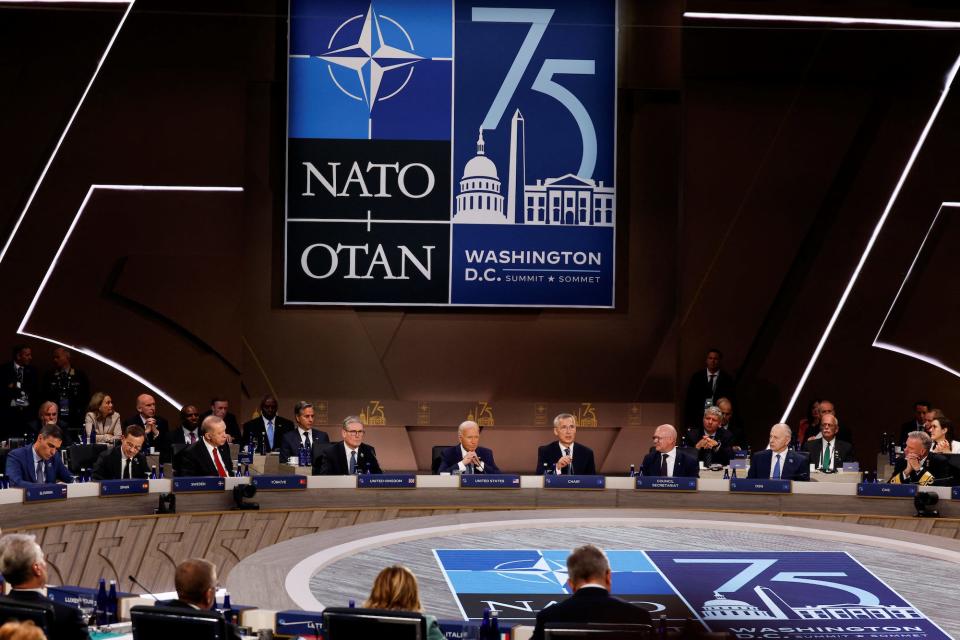 NATO member country leaders  sit under the alliance's sign