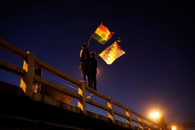 Men wave Bolivian and Wiphala flags as coca farmers and supporters of Bolivia's ousted President Evo Morales stage a blockade of an entrance to Sacaba