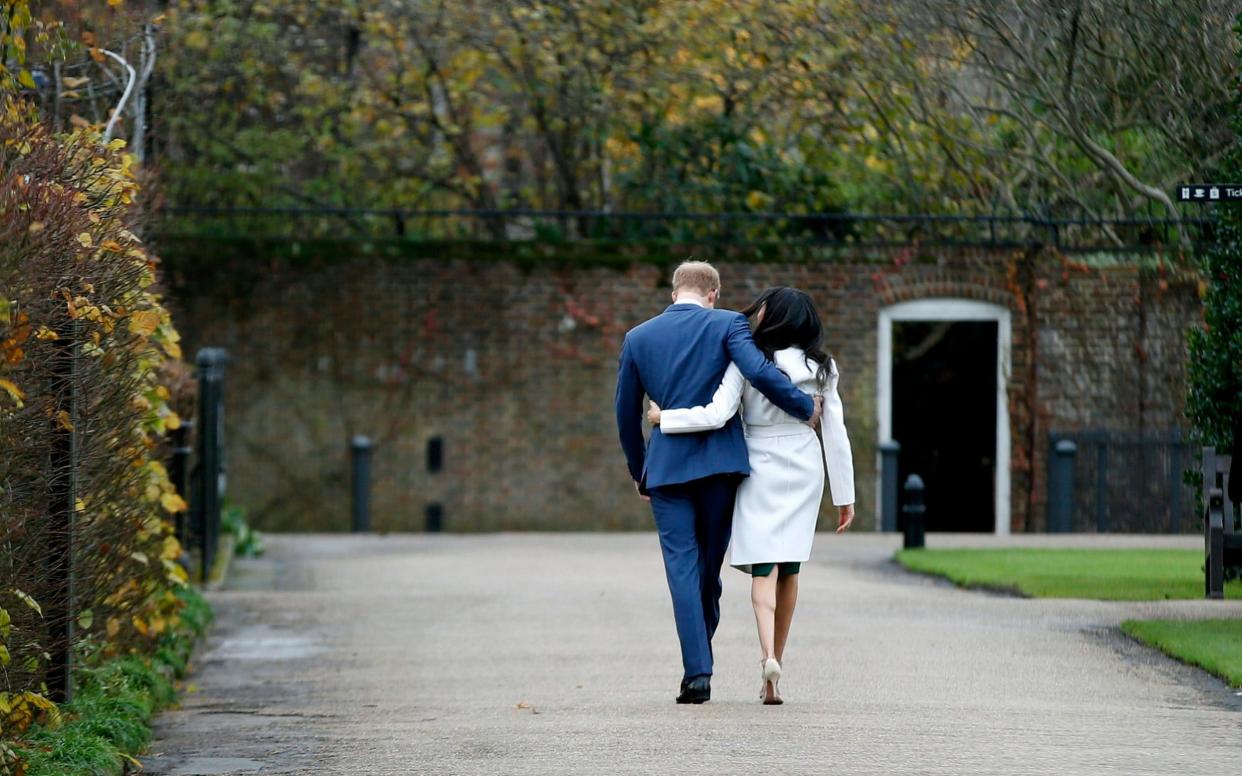 Prince Harry and Meghan Markle walk away after posing for the media in the grounds of Kensington Palace in London - Alastair Grant/AP