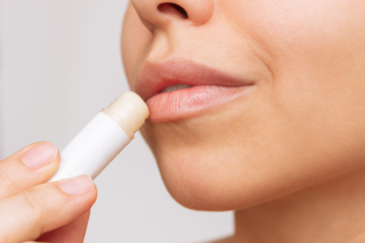 a young woman applying moisturizing chapstick to her lips on a gray background
