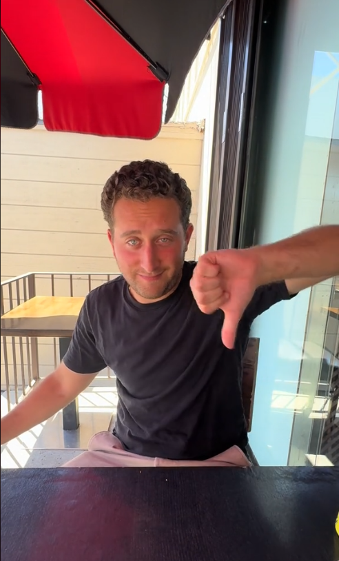 Man at a dining table giving a thumbs-down gesture