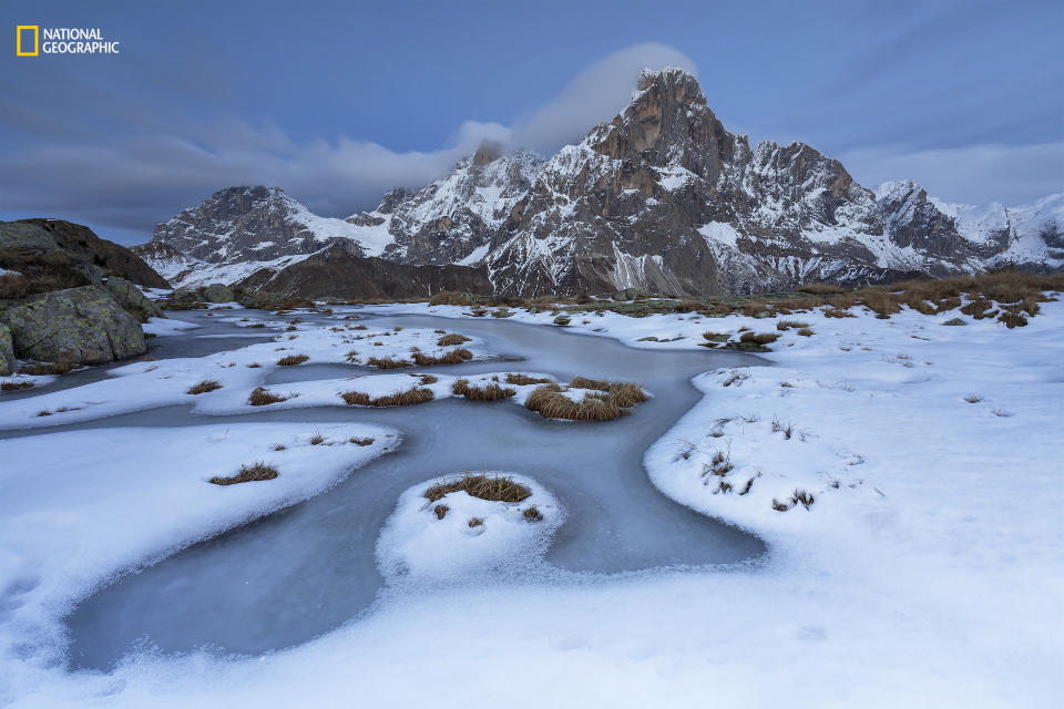 Alessandro Gruzza: "The first cold days of winter have frozen the surface of a pond, and the first snowfall has revealed its delicate beauty. In low-pressure conditions, southwest winds push the clouds against the vertical peaks of the Pale di San Martino. At dusk, a long shutter speed enhances the movement of the clouds around Cimon della Pala, one of the highest peaks in the Dolomites."