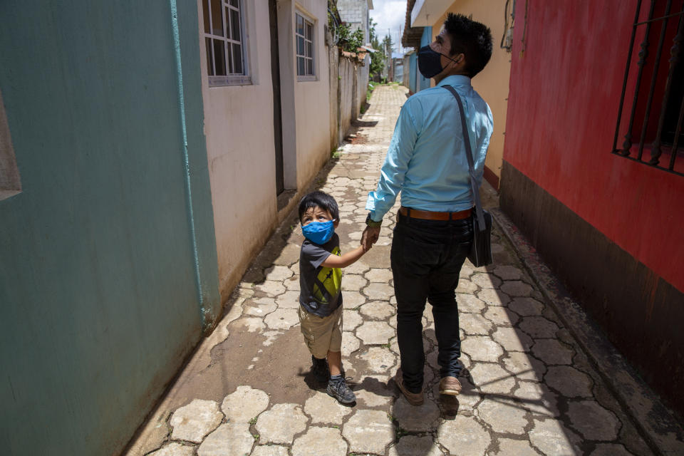 Teacher Gerardo Ixcoy and his three-year-old son Dylan greet a neighbor as Ixcoy arrives home after a day of giving individual instruction to his sixth-grade students, in Santa Cruz del Quiche, Guatemala, Wednesday, July 15, 2020. By afternoon Ixcoy pedals his classroom-on-a-trike for home to beat a mandatory curfew set in place to help curb the spread of the new coronavirus. (AP Photo/Moises Castillo)