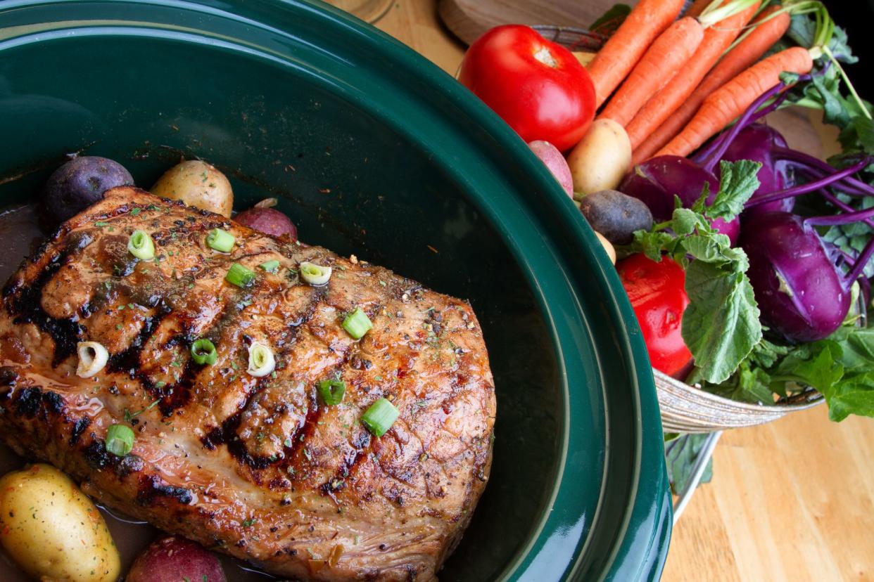 Crock pot full of roasted baby potatos and a delicious pot roast in gravy with fresh vegetables on the side