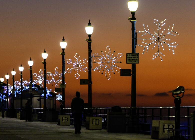 Huntington Beach, CA - December 12: 80 snowflakes light up the Huntington Beach Pier as pier walkers are silhouetted by the sunset's glow amid pleasant weather in Huntington Beach Tuesday, Dec. 12, 2023. (Allen J. Schaben / Los Angeles Times)