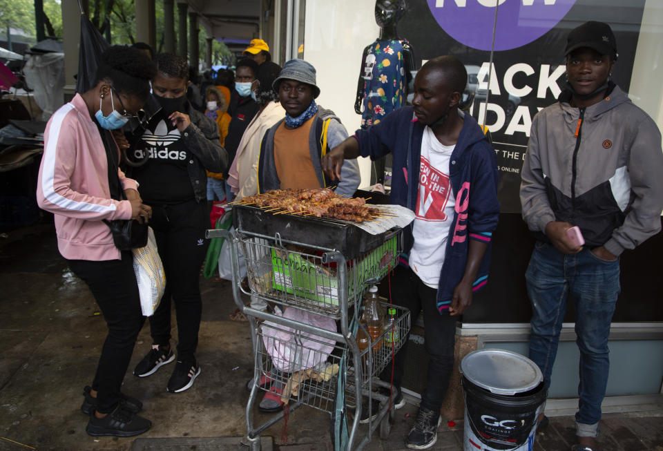 FILE - A woman wearing a face mask to curb the spread of coronavirus buys chicken on a crowded sidewalk in Pretoria, South Africa, Saturday, Nov. 27, 2021. The world is racing to contain a new COVID-19 variant, which appears to be driving a surge in South Africa and is casting a pall there. (AP Photo/Denis Farrell)