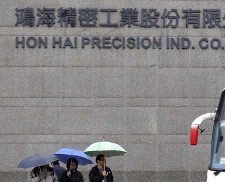 People holding umbrellas walk in front of the headquarters of Hon Hai, which is also known by its trading name Foxconn, in Tucheng, New Taipei city, December 24, 2013. REUTERS/Pichi Chuang