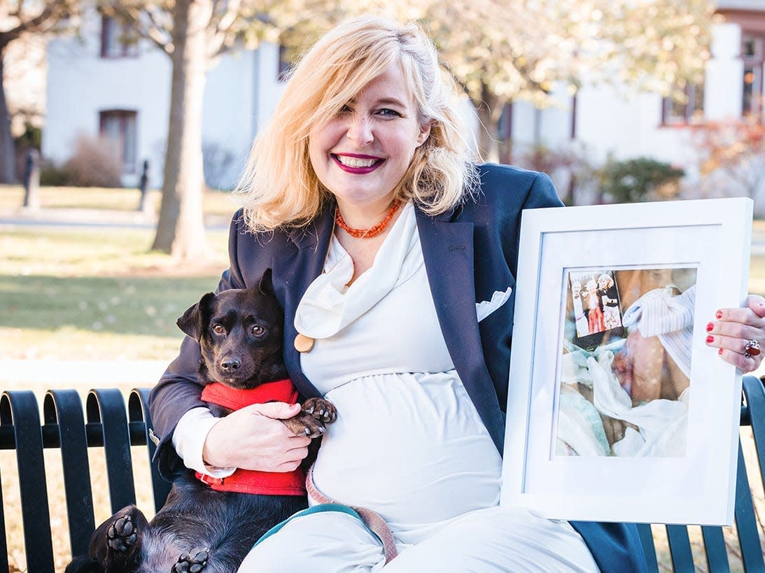 Rachel Unkovic sitting on a bench holding up a picture of her first baby and her dog