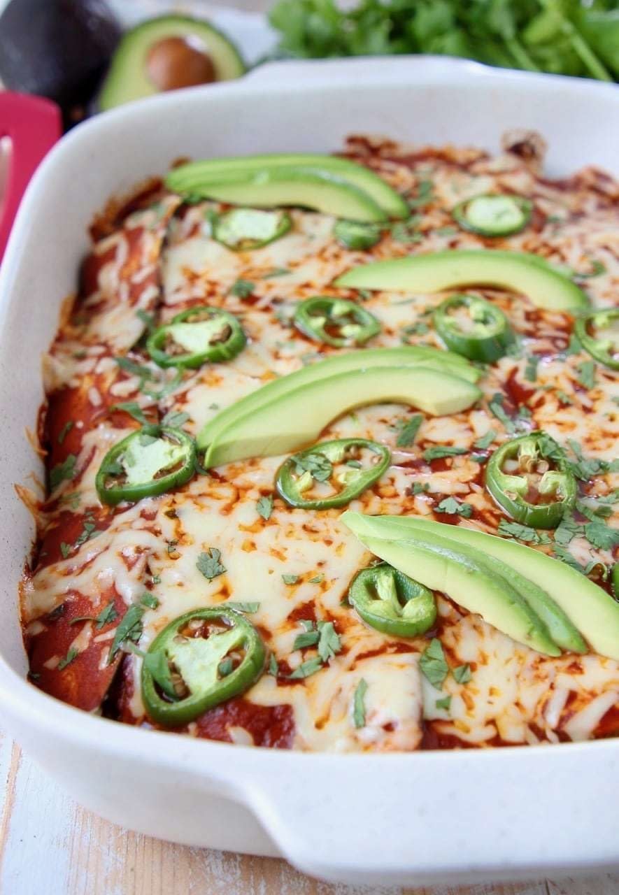 Enchiladas topped with jalapeño slices, avocados, and cilantro in a white baking dish