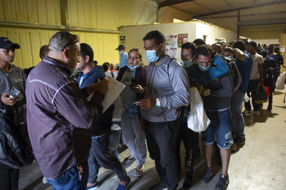 FILE - People line up for a commercial bus that will take them to the San Antonio airport at a warehouse run by the Mission: Border Hope nonprofit group run by the United Methodist Church in Eagle Pass, Texas, May 23, 2022. U.S. immigration authorities are planning to issue photo ID cards to immigrants in deportation proceedings in a bid to slash paper use and help people stay up-to-date on required meetings and court hearings, officials said. (AP Photo/Dario Lopez-Mills, File)