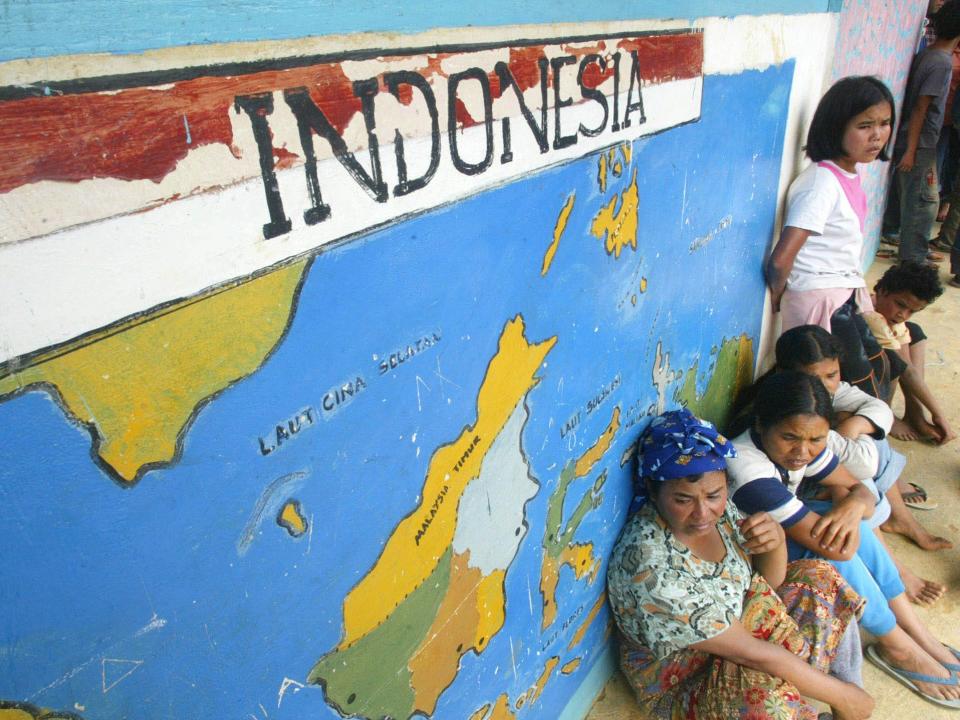 Villagers sit near a map of Indonesia painted on the wall at a school.