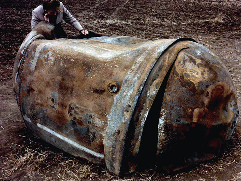 A woman on her cell phone leans over to inspect a large piece of fallen space debris.