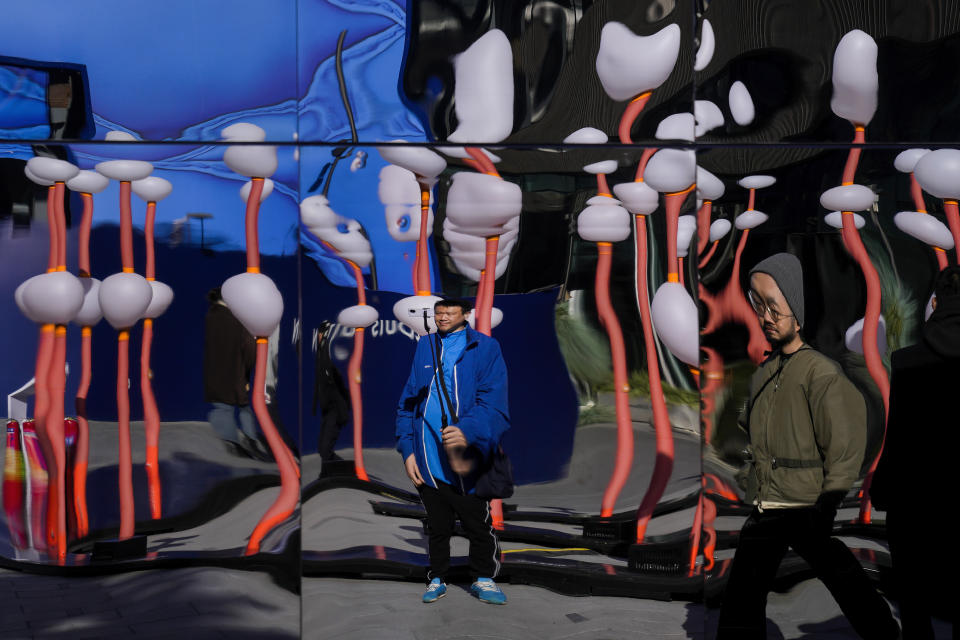 A man is reflected on a distortion panels as he takes a selfie with a lights display at an outdoor shopping mall in Beijing, Sunday, Nov. 12, 2023. (AP Photo/Andy Wong)