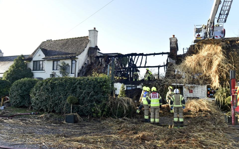 Firemen stand outside the shell of a burned down building, mostly reduced to a charred wooden frame - Yorkshire Post / SWNS