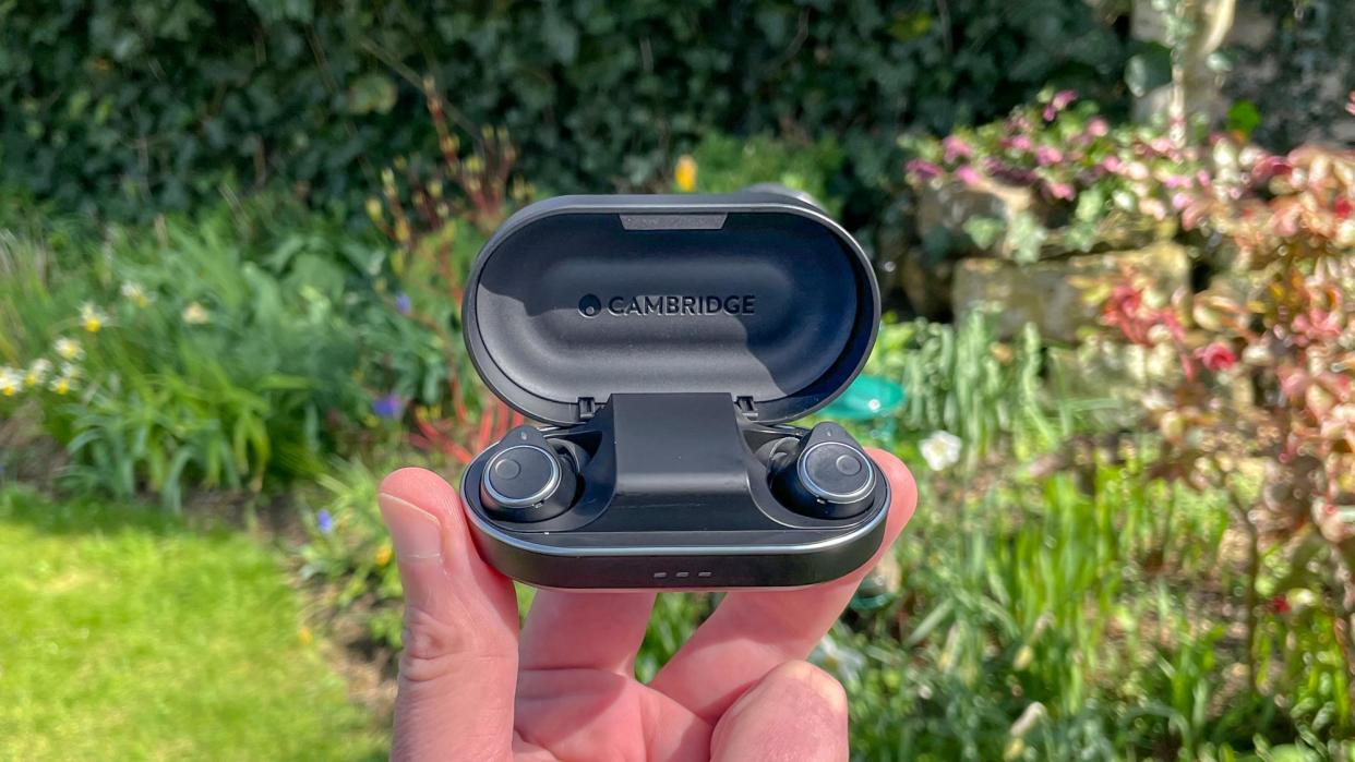  Cambridge Audio Melomania M100 in charging case held in hand in a yard. 