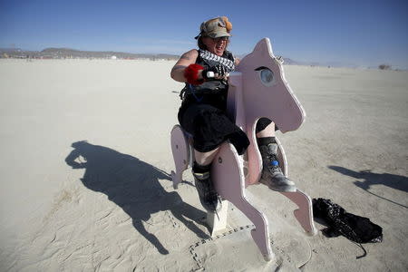 Kentucky Sunshine, her Playa name, rides a rocking horse art installation during the Burning Man 2015 "Carnival of Mirrors" arts and music festival in the Black Rock Desert of Nevada, September 1, 2015. REUTERS/Jim Urquhart