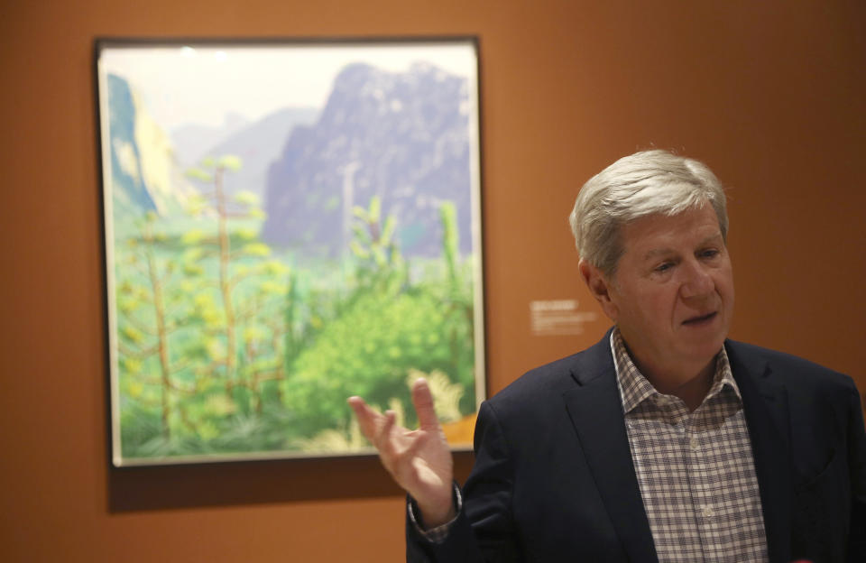 In this Wednesday, Oct. 23, 2019, photo, Richard Benefield, former executive director of the David Hockney Foundation, talks about the exhibit of Hockney's Yosemite artistic work, background, along with baskets from weavers from the Miwok and Mono Lake Paiute tribes on display at the Heard Museum in Phoenix. "David Hockney's Yosemite and Masters of California Basketry" exhibition opens Monday. (AP Photo/Ross D. Franklin)