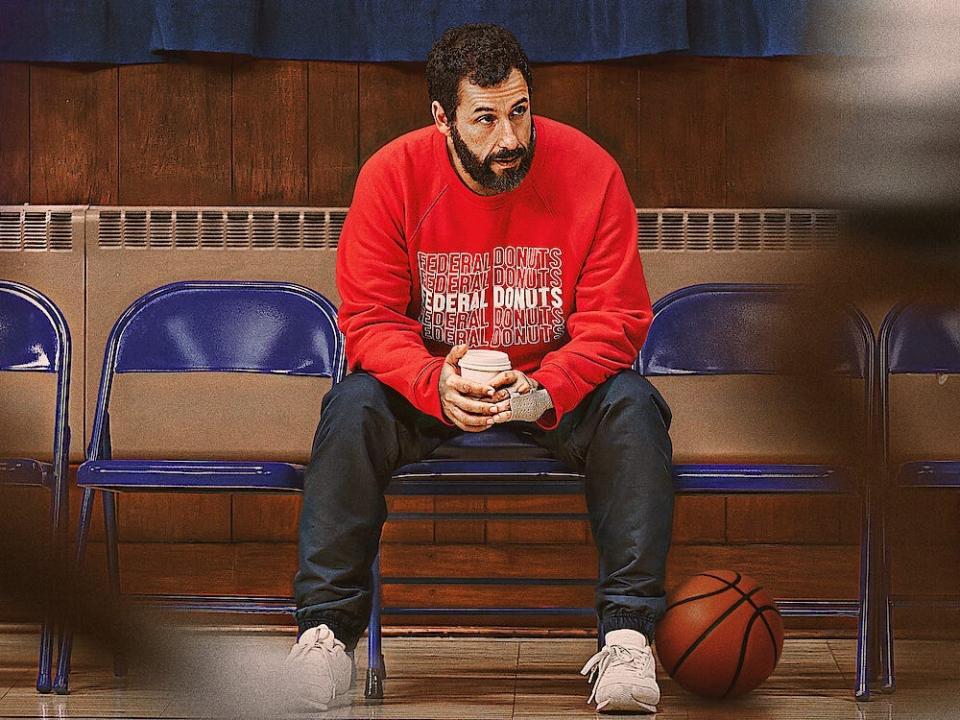 Adam Sandler sitting holding a coffee cup