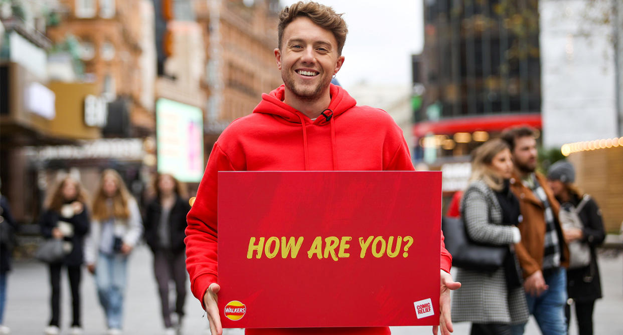 Roman Kemp holding a sign saying 'how are you?' (SWNS)