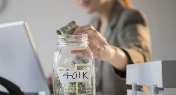 Businesswoman putting money into 401K jar at desk