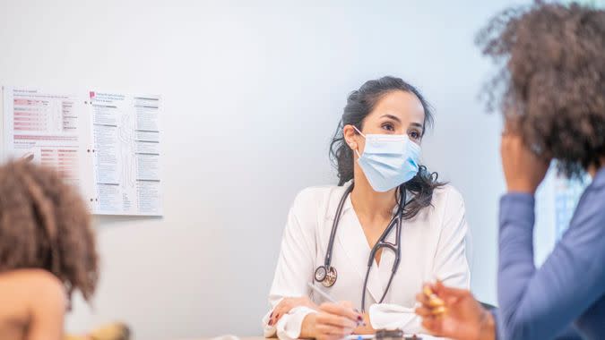 A mother and her daughter sit in a doctor's office and consult with their doctor.