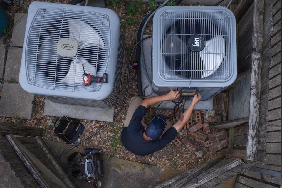 man wearing blue shirt and hat works on panel on the side of a large outdoor air conditioning unit