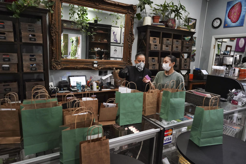 In this Thursday, April 16, 2020, photo, wearing a protective mask and gloves, budtenders prepare orders for customers to pick-up at The Higher Path cannabis dispensary in the Sherman Oaks section of Los Angeles. Monday is April 20, or 4/20. That’s the code for marijuana’s high holiday, which is usually marked with outdoor festivals and communal smoking sessions. But this year, stay-at-home orders have moved the party online as the marijuana market braces for an economic blow from the coronavirus crisis. (AP Photo/Richard Vogel)