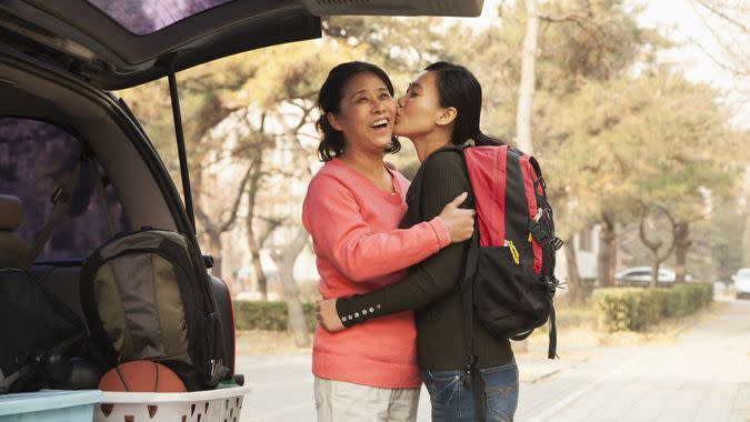 Mother and daughter embracing behind car on college campus stock photo