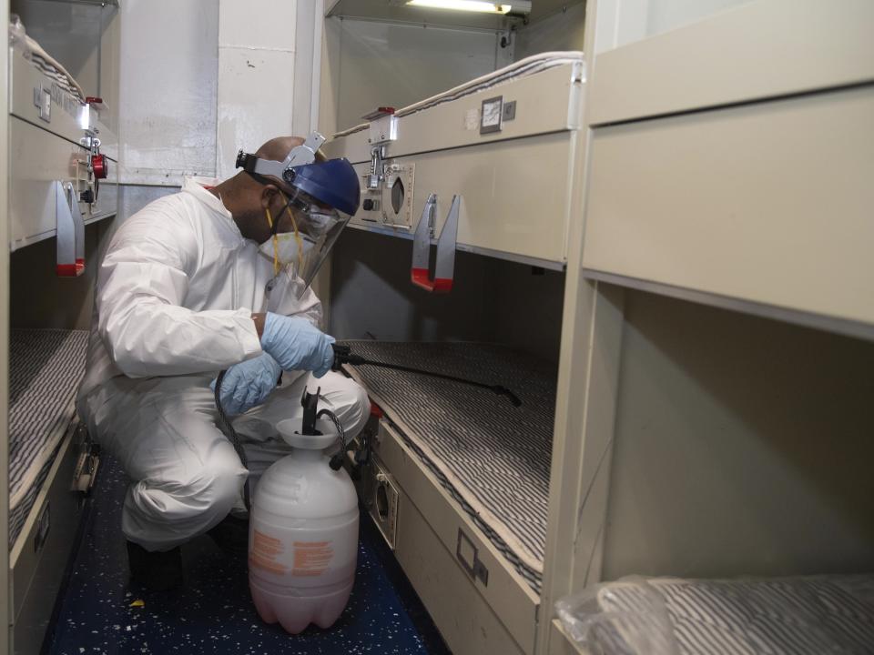 FILE - In this April 12, 2020, file photo provided by the U.S. Navy, U.S. Navy Aviation Ordnanceman Airman Brian Miller, of Mineral Wells, Texas, disinfects a berthing aboard the aircraft carrier USS Theodore Roosevelt (CVN 71) with a multi-surface sanitizer. The U.S. Navy says that after weeks of work, all of the roughly 4,800 sailors on the coronavirus-stricken USS Theodore Roosevelt aircraft carrier have been tested for the virus. The ship has been sidelined in Guam since March 27, moving sailors ashore, testing them and isolating them for nearly a month.(Mass Communication Specialist Seaman Kaylianna Genier/U.S. Navy via AP, File)