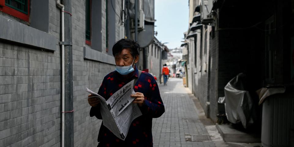 An elderly man reads a newspaper while walking in an alley in Beijing on May 9, 2022.