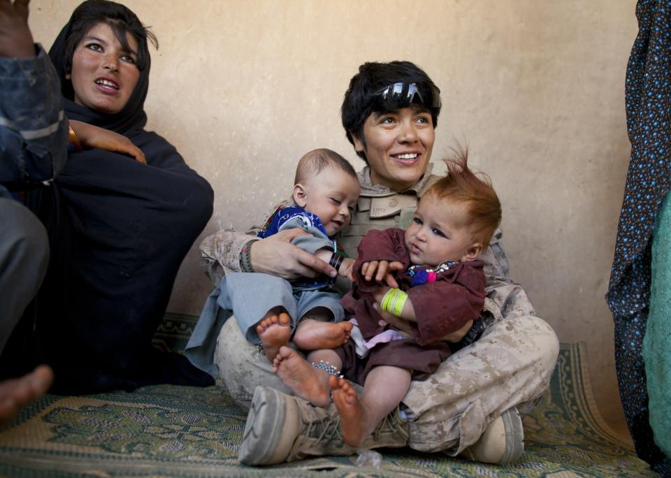 BOLDOC, AFGHANISTAN - NOVEMBER 23: Lance Corporal Luz Lopez, 21, a US Marine with the FET ( Female Engagement Team) 1st Battalion 8th Marines, Regimental Combat team II plays with Afghan babies during a village medical outreach November 23, 2010 in Boldoc, in Helmand province , Afghanistan. There are 48 women presently working along the volatile front lines of the war in Afghanistan; deployed as the second Female Engagement team participating in a more active role, gaining access where men can't. The women, many who volunteer for the 6.5 month deployment, take a 10 week course at Camp Pendleton in California where they are trained for any possible situation, including learning Afghan customs and basic Pashtun language. (Photo by Paula Bronstein/Getty Images)