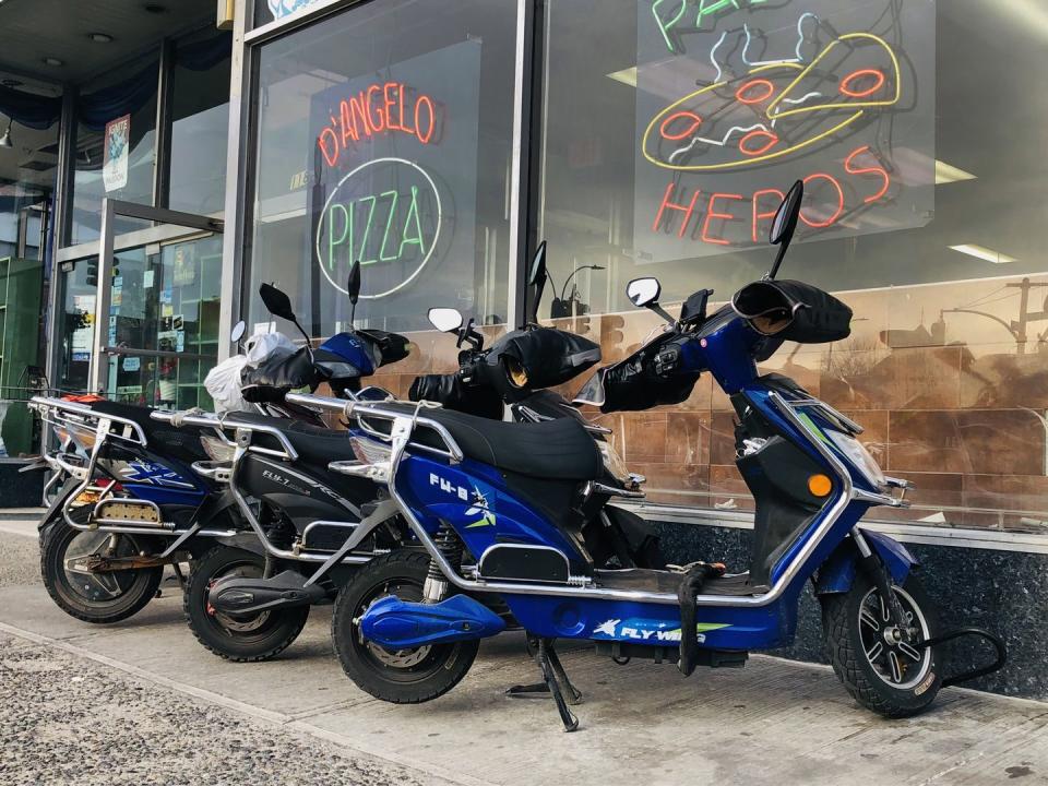 several electric scooters used for food delivery parked in front of d'angelo pizza and hero restaurant, queens, new york