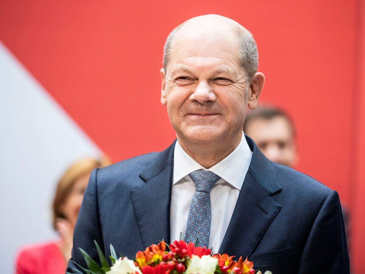 Olaf Scholz, wearing a suit and carrying a bouquet of flowers smiles after his party, the SPD, gathered the most votes in Germany's preliminary elections  results
