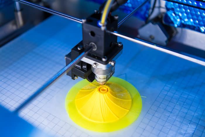 A 3D printer printing a yellow plastic object.