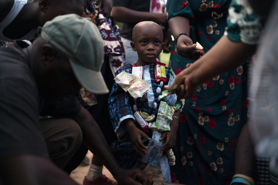 Wearing a collar of candies and money, 3-year-old Kebba Sarr takes part in the initiation rites during the Kankurang ritual in Bakau, Gambia, Saturday, Oct. 2, 2021. Relatives and friends offer small amounts of money, as a sign of gratitude. Kankurang, as guarantor of order and justice and protector against the evil spirits, ensures transmission and teaching of the Mandinka cultural identity. (AP Photo/Leo Correa)