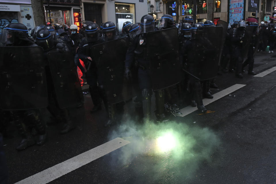 A flare explodes by a line of riot police officers during a protest, Saturday, Dec.12, 2020 in Paris. Protests are planned in France against a proposed bill that could make it more difficult for witnesses to film police officers. (AP Photo/Thibault Camus)