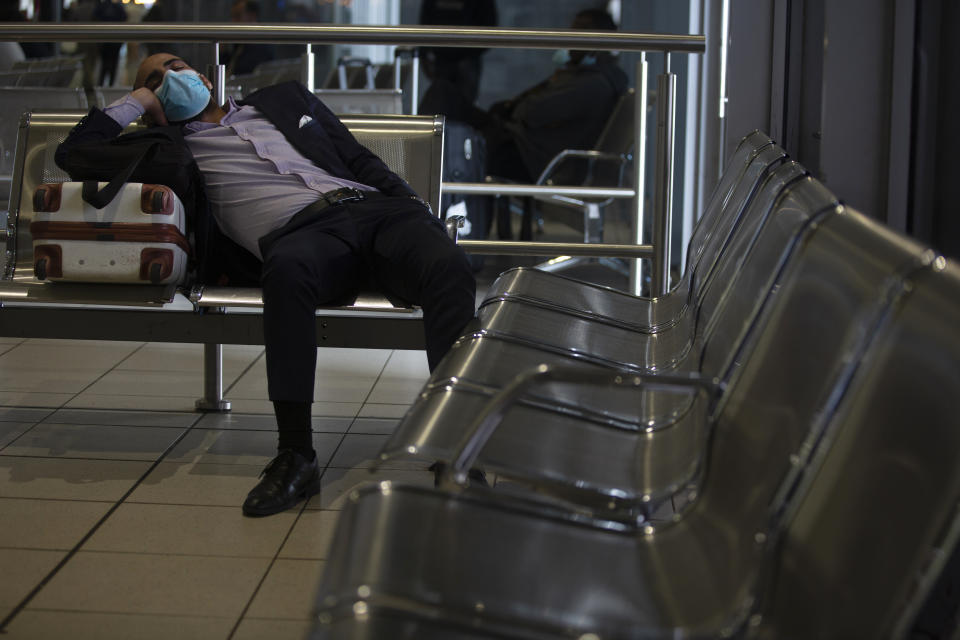 A traveller wearing a mask sits in Johannesburg's O.R. Tambo International Airport, Monday, March 16, 2020, a day after President Cyril Ramaphosa declared a national state of disaster. Ramaphosa said all schools will be closed for 30 days from Wednesday and he banned all public gatherings of more than 100 people. South Africa will close 35 of its 53 land borders and will intensify screening at its international airports. For most people, the new COVID-19 coronavirus causes only mild or moderate symptoms. For some it can cause more severe illness. (AP Photo/Denis Farrell)