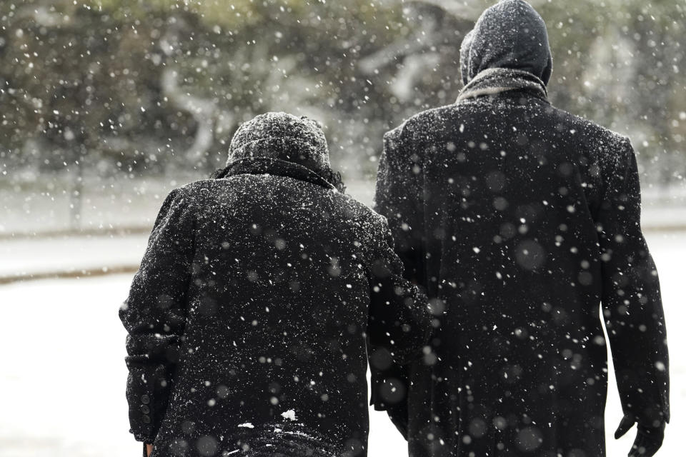 A couple walk through falling snow, Thursday, Feb. 18, 2021, in downtown San Antonio. Snow, ice and sub-freezing weather continue to wreak havoc on the state's power grid and utilities. (AP Photo/Eric Gay)