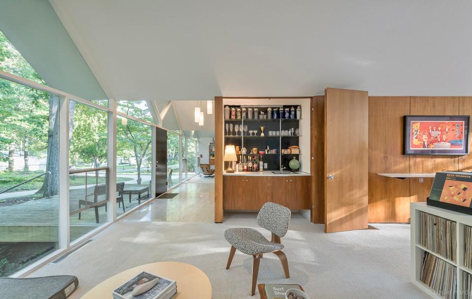A wet bar is seen behind a wooden panel after entering the living room area of a mid-century modern house in Farmington Hills, designed by award-winning architect William Kessler for carpet and flooring mogul Arthur Beckwith in 1960. There are two living room areas to the left and right of the entrance.