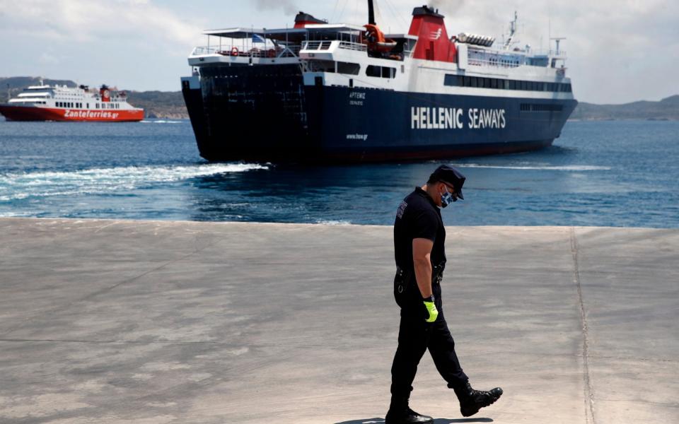 A coast guard officer wearing a face mask to prevent the spread of the new coronavirus, walks on the dock as a ferry, right, leaves and another one approaches the Aegean Sea island of Milos, Greece - AP
