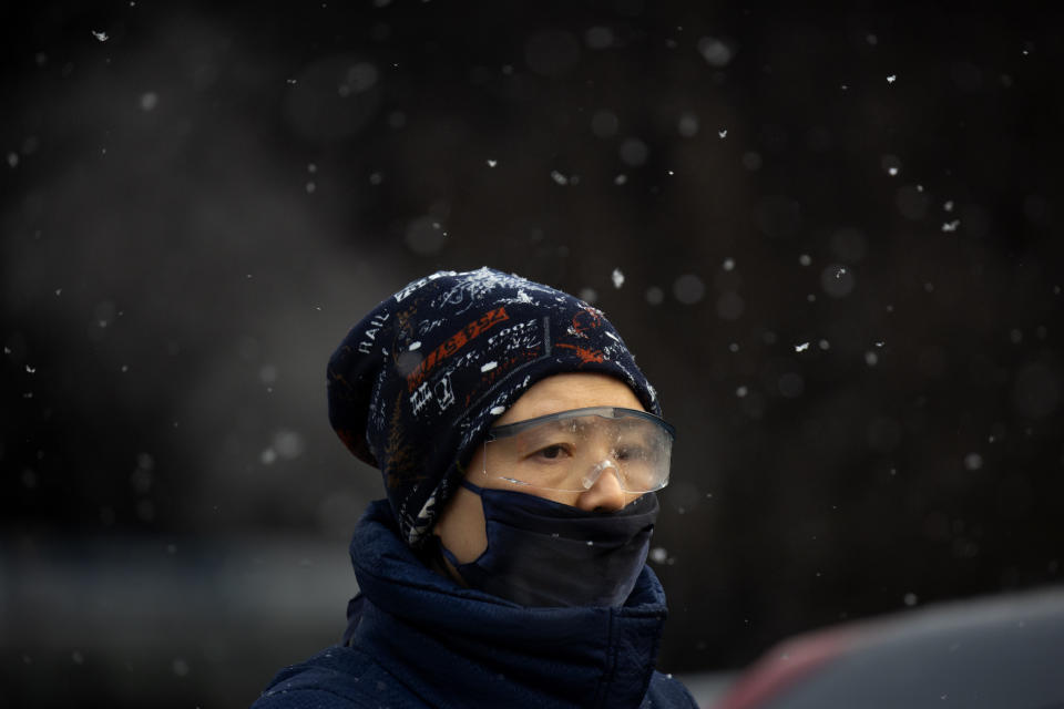 A man wearing a face mask to protect against the spread of the coronavirus waits at an intersection during a snowy morning in Beijing, Tuesday, Jan. 19, 2021. A Chinese province near Beijing grappling with a spike in coronavirus cases is reinstating tight restrictions on weddings, funerals and other family gatherings, threatening violators with criminal charges. (AP Photo/Mark Schiefelbein)