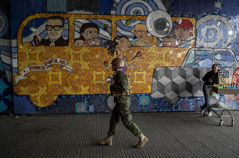 Chilean Army soldier walks in front a mural representing late chilean President Salvador Allende while guarding a subway station during a second day protests in Santiago, Chile, Saturday, Oct. 19, 2019. The protests started on Friday afternoon when high school students flooded subway stations, jumping turnstiles, dodging fares and vandalizing stations as part of protests against a fare hike, but by nightfall had extended throughout Santiago with students setting up barricades and fires at the entrances to subway stations, forcing President Sebastian Pinera to announce a state of emergency and deploy the armed forces into the streets. (AP Photo/Esteban Felix)